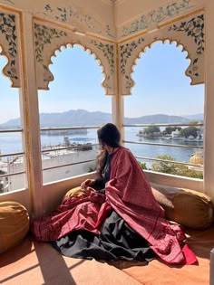 a woman sitting on top of a bed in front of a window next to a body of water