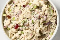 a white bowl filled with chicken salad on top of a marble counter next to a silver spoon