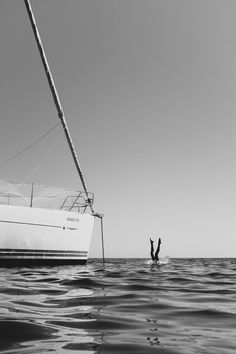 a person on a surfboard in the water near a sailboat that is upside down