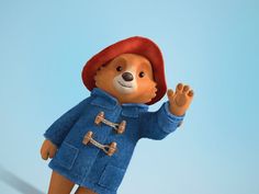 a brown teddy bear wearing a blue coat and red hat standing in front of a blue background