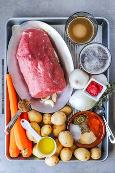 raw meat, potatoes, carrots, garlic and seasonings on a metal tray