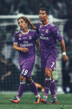 two soccer players in purple uniforms are walking on the field with their arms around each other