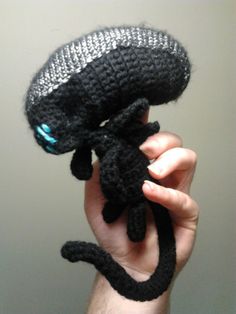 a hand holding up a black crocheted stuffed animal