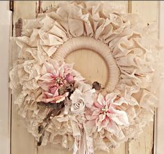 a white wreath with pink flowers hanging on a door handle and shabby lace around it