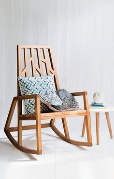 a wooden rocking chair sitting next to a table with a pillow on top of it