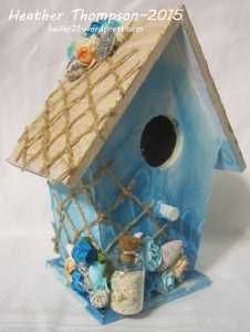 a blue birdhouse with flowers and shells in it