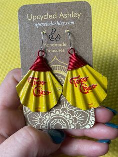 a pair of yellow fan - shaped earrings with red lettering on the front and bottom