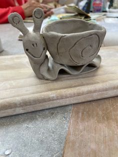 a clay animal sitting on top of a wooden cutting board next to a bowl filled with water