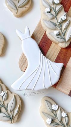 cookies decorated with white flowers and leaves are on a cutting board next to other cookies