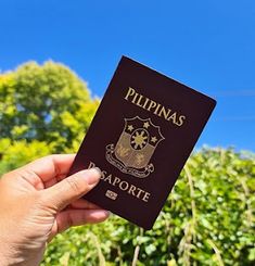 a person holding up a passport in front of some bushes and trees on a sunny day