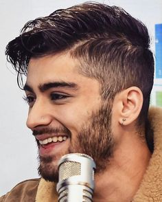 a close up of a person with a microphone in front of a white wall and smiling