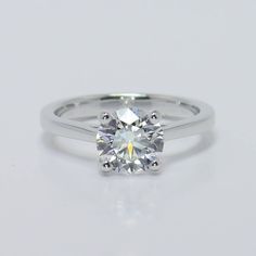 a white gold engagement ring with a round brilliant cut diamond in the center, on a plain surface