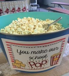 a bowl filled with popcorn sitting on top of a table next to a sign that says, you make our school pop