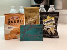 four different types of snacks sitting on a counter next to bottles of water and a bag of chips