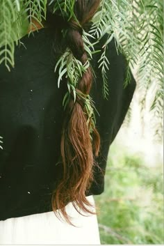 a woman with long red hair is standing in front of some trees and has her back turned to the camera