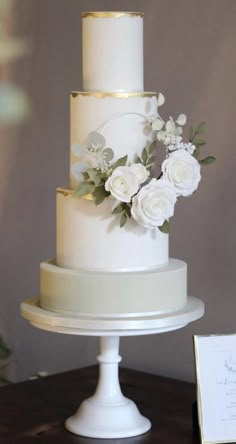 a three tiered white wedding cake with flowers on the top and bottom, sitting on a table