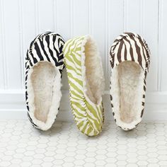 three zebra print slippers lined up against a wall with the words cozy toes written on them