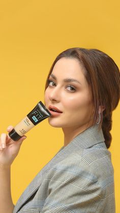 a woman holding up a tube of makeup to her face and looking at the camera