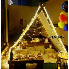 a table topped with plates and pizza next to a lit up teepee tent filled with balloons