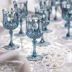 many blue glass goblets are lined up on a white tablecloth with snowflakes