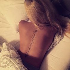 a woman laying in bed with her back turned to the camera and tattoos on her lower back