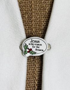 jesus is the reason for the season pin on a white sweater with holly decorations around it