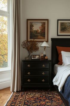 a bed sitting next to a window with a painting on it's wall above it