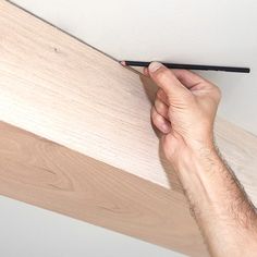 a man is holding a pencil over a piece of wood