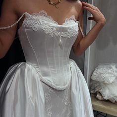 a woman in a white wedding dress is holding her hand up to her face and looking at the mirror