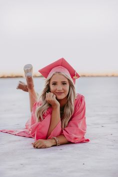 a woman laying on the ground wearing a pink graduation gown and holding a coffee cup