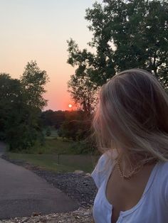 a woman standing on the side of a road at sunset with her hair blowing in the wind