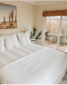 a bed with white sheets and pillows in a bedroom next to a sliding glass door