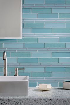 a bathroom sink sitting under a mirror next to a faucet in front of a blue tiled wall