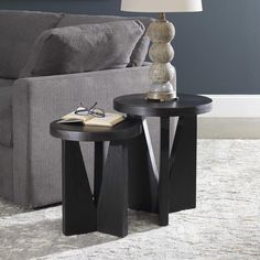 two end tables sitting on top of a carpeted floor next to a gray couch