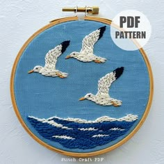 three seagulls flying over the ocean in blue and white embroidery on a hoop