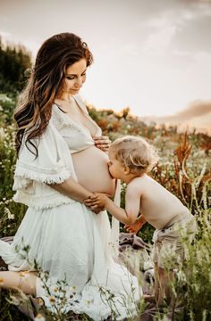 a pregnant woman in a white dress is holding her child's belly as they sit on the ground