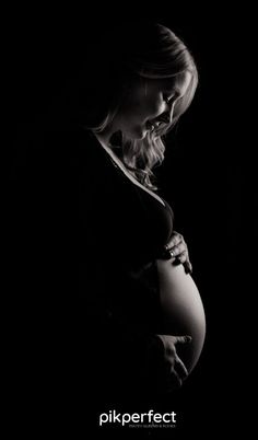 a pregnant woman in the dark with her hands on her belly