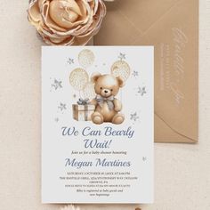 a teddy bear holding a gift box on top of a card next to a flower