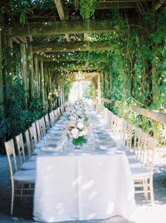 a long table is set up with white linens and place settings for an outdoor dinner