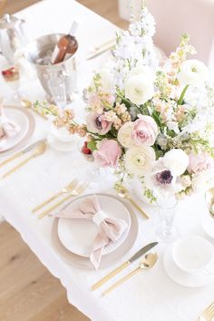 a white table topped with lots of pink and white flowers next to gold place settings