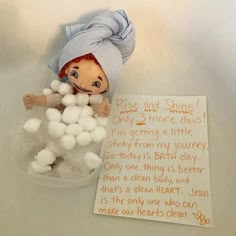 a small doll sitting in a tub filled with cotton balls next to a note that says rise and shine only 2 more days