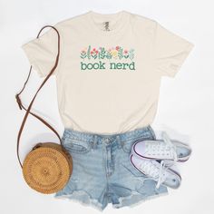 Featuring the words "Book Nerd" in a timeless typewriter font, this Comfort Colors T-shirt celebrates a reader's love of literature in style. Pretty flowers adorn the text making it as stylish as it is soft and comfy. This cute book shirt is a perfect addition to any book lover's wardrobe.! Want to spend every day in the comfort of Saturday morning? Slip on a Comfort Colors 1717 Adult Tee and enjoy the softness of 100% USA-grown ring-spun cotton. The fabric is garment-washed until it's as cozy as if you had worn it fifty times. Available Sizes: S-4XL Pigment Dye Colors: These colors provide a vintage look that will remain for the life of the garment Material: 100% Ring Spun US Cotton, Pre-Shrunk Fit: Relaxed Care: Machine Wash Cold Summer Bookish T-shirt With Letter Print, Bookish Cotton T-shirt With Letter Print, Summer Graphic Print Bookish T-shirt, Bookish Short Sleeve T-shirt For Spring, Spring Bookish Short Sleeve T-shirt, Spring Bookish Style Short Sleeve T-shirt, Bookish Short Sleeve Tops For Spring, Spring Bookish Short Sleeve Tops, Bookish Cotton T-shirt With Funny Print