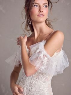 a beautiful young woman in a white dress posing for a photo with her hand on her shoulder