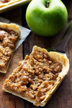 two pieces of apple pie sitting on top of a wooden table next to an apple