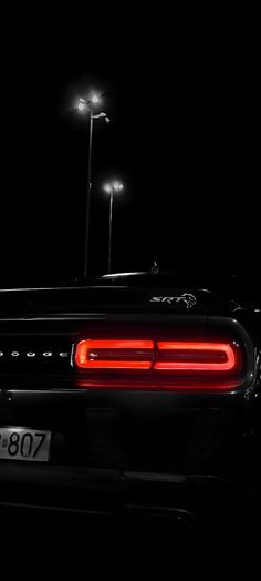 the rear end of a black sports car at night with street lights in the background