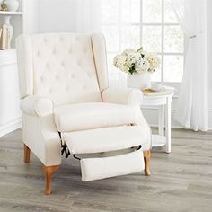 a white chair and footstool in front of a window with flowers on it