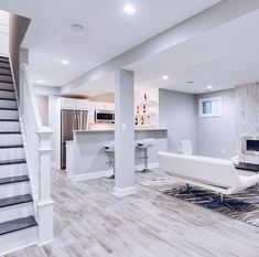 a living room filled with furniture and a staircase leading up to the top floor in front of a kitchen