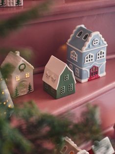 three small houses sitting on top of a pink shelf next to a christmas ornament