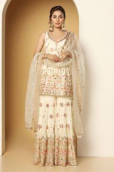 Ivory sleeveless padded short kurta in georgette base with all over mughal bloom multi color thread, zari, mirror embroideries, sequin highlights and paan neckline. Paired with a floral motif embroidered sharara and mirror border embellished net dupatta. - Aza Fashions White Sleeveless Festive Sharara, Festive Sleeveless White Sharara, Fitted Sleeveless White Sharara, White Sleeveless Sharara For Festive Occasion, Mirror Border, Embroidered Sharara, Kurta Sharara Set, Kurta Sharara, Short Kurta