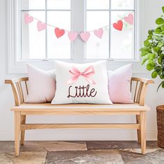 a wooden bench sitting in front of a window filled with pink hearts and a pillow that says little